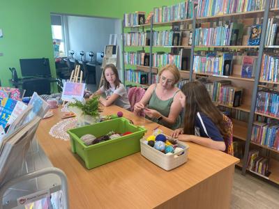 Zdjęcie przedstawia uczestników akcji Dzień Dziergania w Miejscach Publicznych. Zdjęcie wykonano w bibliotece.