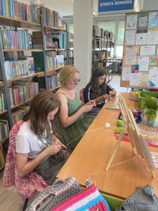 Zdjęcie przedstawia uczestników akcji Dzień Dziergania w Miejscach Publicznych. Zdjęcie wykonano w bibliotece.