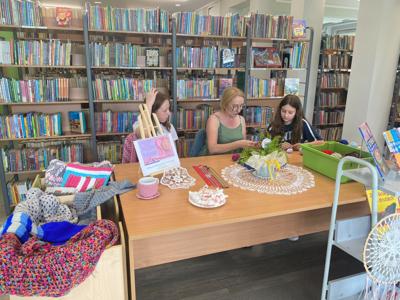 Zdjęcie przedstawia uczestników akcji Dzień Dziergania w Miejscach Publicznych. Zdjęcie wykonano w bibliotece.