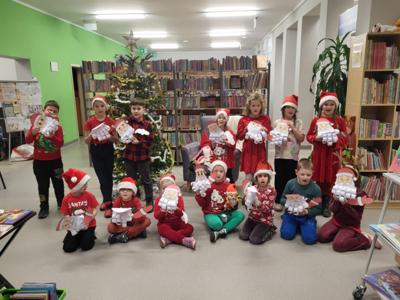 Na zdjęciu znajdują się dzieci trzymające w ręce Mikołaje. W tle książki. Zdjęcie wykonano w bibliotece.