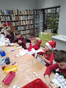 Na zdjęciu znajdują się dzieci siedzące przy stołach. Zdjęcie wykonano w bibliotece.