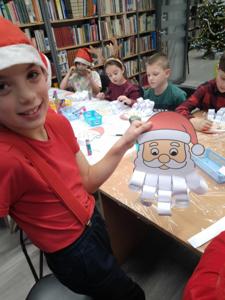 Na zdjęciu znajdują się dzieci siedzące przy stołach. Zdjęcie wykonano w bibliotece.