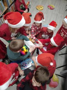 Na zdjęciu znajdują się dzieci, które wyciągają przedmioty z worka. Zdjęcie wykonano w bibliotece.