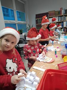 Na zdjęciu znajdują się dzieci siedzące przy stołach. Zdjęcie wykonano w bibliotece.