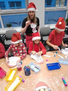 Na zdjęciu znajdują się dzieci siedzące przy stołach. Zdjęcie wykonano w bibliotece.