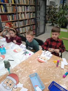 Na zdjęciu znajdują się dzieci siedzące przy stołach. Zdjęcie wykonano w bibliotece.