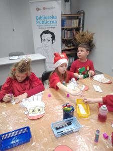 Na zdjęciu znajdują się dzieci siedzące przy stołach. Zdjęcie wykonano w bibliotece.