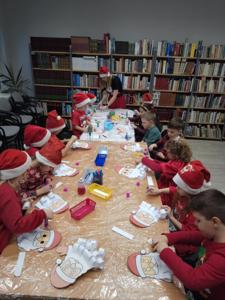 Na zdjęciu znajdują się dzieci siedzące przy stołach. Zdjęcie wykonano w bibliotece.