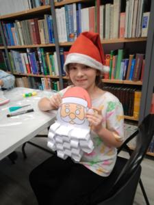 Na zdjęciu znajdują się dzieci siedzące przy stołach. Zdjęcie wykonano w bibliotece.