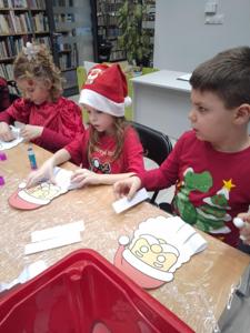 Na zdjęciu znajdują się dzieci siedzące przy stołach. Zdjęcie wykonano w bibliotece.