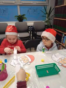 Na zdjęciu znajdują się dzieci siedzące przy stołach. Zdjęcie wykonano w bibliotece.