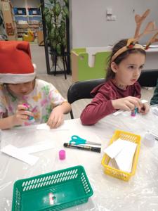 Na zdjęciu znajdują się dzieci siedzące przy stołach. Zdjęcie wykonano w bibliotece.