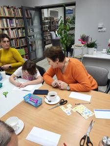 Na zdjęciu znajdują się uczestnicy zajęć. Uczestnicy siedzą. W tle książki.