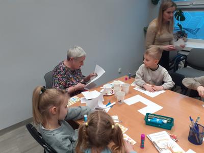 Na zdjęciu znajdują się uczestnicy zajęć. Uczestnicy siedzą. W tle książki.