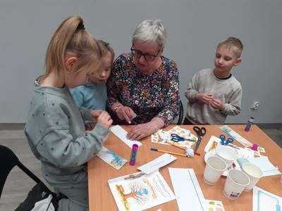 Na zdjęciu znajdują się uczestnicy zajęć. Uczestnicy siedzą. W tle książki.