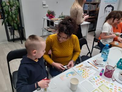 Na zdjęciu znajdują się uczestnicy zajęć. Uczestnicy siedzą. W tle książki.