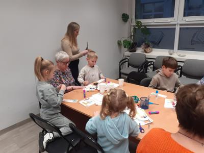 Na zdjęciu znajdują się uczestnicy zajęć. Uczestnicy siedzą. W tle książki.