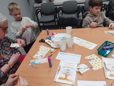 Na zdjęciu znajdują się uczestnicy zajęć. Uczestnicy siedzą. W tle książki.