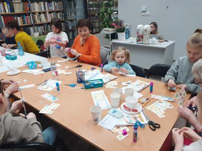 Na zdjęciu znajdują się uczestnicy zajęć. Uczestnicy siedzą. W tle książki.