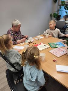 Na zdjęciu znajdują się uczestnicy zajęć. Uczestnicy siedzą. W tle książki.