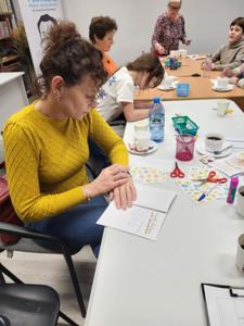 Na zdjęciu znajdują się uczestnicy zajęć. Uczestnicy siedzą. W tle książki.