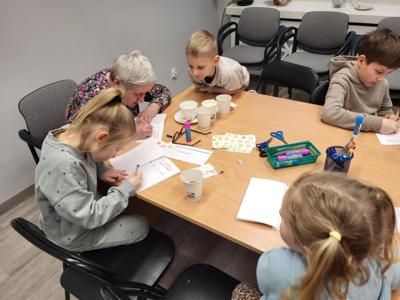 Na zdjęciu znajdują się uczestnicy zajęć. Uczestnicy siedzą. W tle książki.