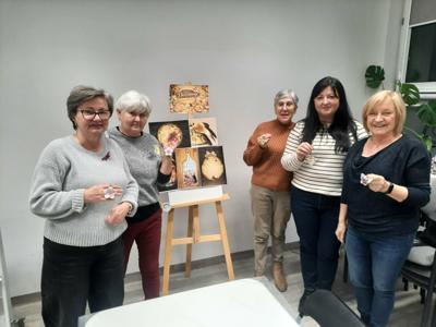 Na zdjęciu znajdują się Panie trzymające drewniane przedmioty. Zdjęcie wykonano w bibliotece.