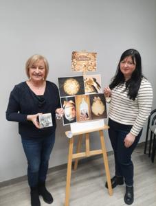 Na zdjęciu znajdują się Panie trzymające drewniane przedmioty. Zdjęcie wykonano w bibliotece.