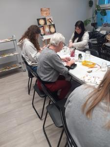 Na zdjęciu znajdują się Panie trzymające drewniane przedmioty. Zdjęcie wykonano w bibliotece.