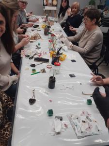 Na zdjęciu znajdują się Panie trzymające drewniane przedmioty. Zdjęcie wykonano w bibliotece.