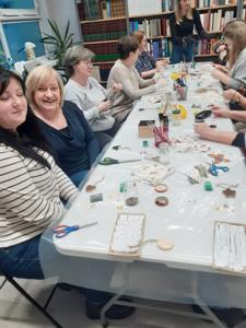 Na zdjęciu znajdują się Panie trzymające drewniane przedmioty. Zdjęcie wykonano w bibliotece.