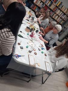 Na zdjęciu znajdują się Panie trzymające drewniane przedmioty. Zdjęcie wykonano w bibliotece.