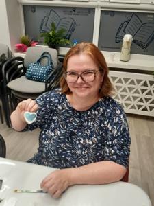 Na zdjęciu znajdują się Panie trzymające drewniane przedmioty. Zdjęcie wykonano w bibliotece.