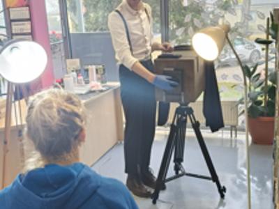 Fotograf odkrywa dekielek aparatu naprzeciw kobiety pozującej do zdjęcia.