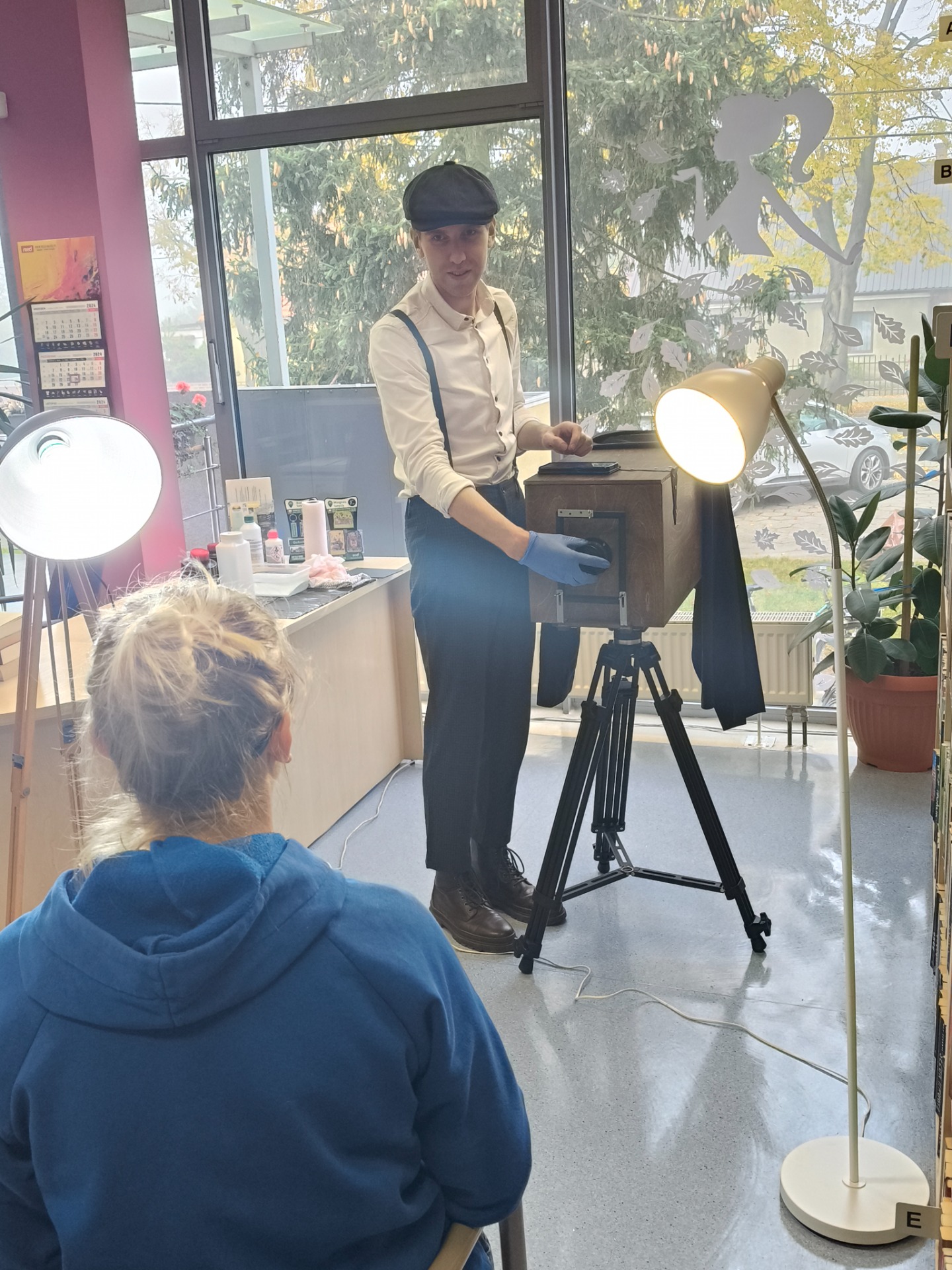 Fotograf odkrywa dekielek aparatu naprzeciw kobiety pozującej do zdjęcia.