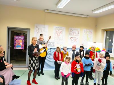 Kaja Król-Brandyk trzyma mikrofon, dzieci ustawione do występu