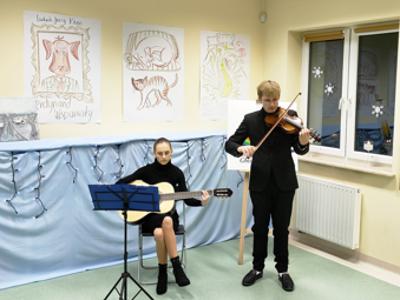 Siedząca dziewczyna z gitarą, chłopak stoi ze skrzypcami