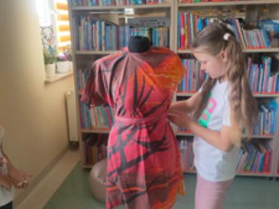 dziewczynka poprawia czerwoną suknię na manekinie