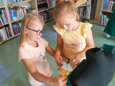 Dwie dziewczynki przymierzają zielony materiał do czarnego manekina