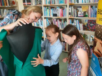 Natalia Zawartka-Ignaszak pomaga dwóm dziewczynkom w projekcie zielonej sukni na czarnym manekinie