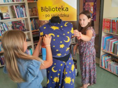 Dwie dziewczynki poprawiają górę sukni z niebieskiego materiału w księżyce i gwiazdki na czarnym manekinie