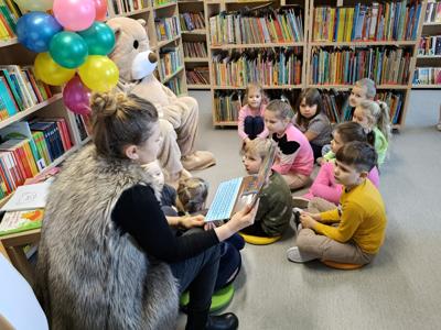 Pani bibliotekarka czyta książkę dzieciom przy misiu.