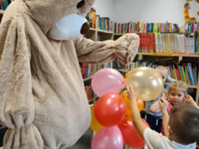 Miś trzyma balony, gdy dzieci rozbijają je wykałaczką