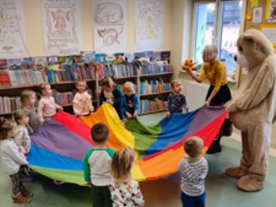 Miś, pani bibliotekarka i dzieci trzymają chustę.