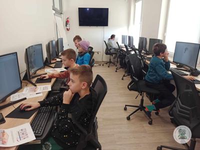 Uczestnicy siedzą przy komputerach podczas zajęć z projektowania graficznego dla dzieci.