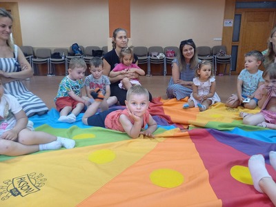 Grupa dzieci oraz rodziców siedzących na kolorowej chuście
