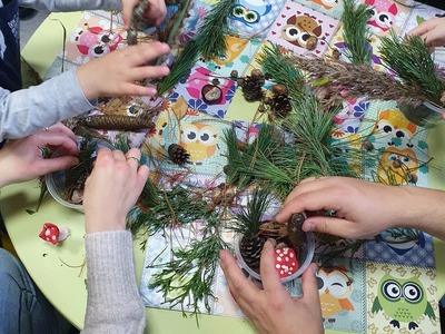 dzieci siedzące przy stoliku,wykonują kompozycje z żywych gałązek drzew