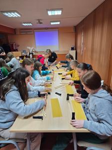 grupa dzieci siedząca przy stole i robiąca ramki do ula z miodem