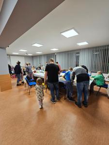 Na zdjęciu grupa ludzi stojąca przy stolikach i chodząca po sali