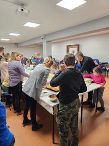 Na zdjęciu grupa ludzi stojących przy stolikach i krojących warzywa i owoce na sałatkę